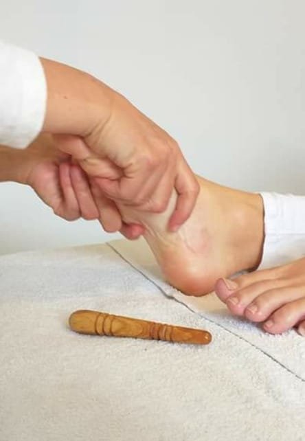Une femme reçoit un foot massaage thaï avec un bâton en bois, illustrant une technique de shiatsu relaxante